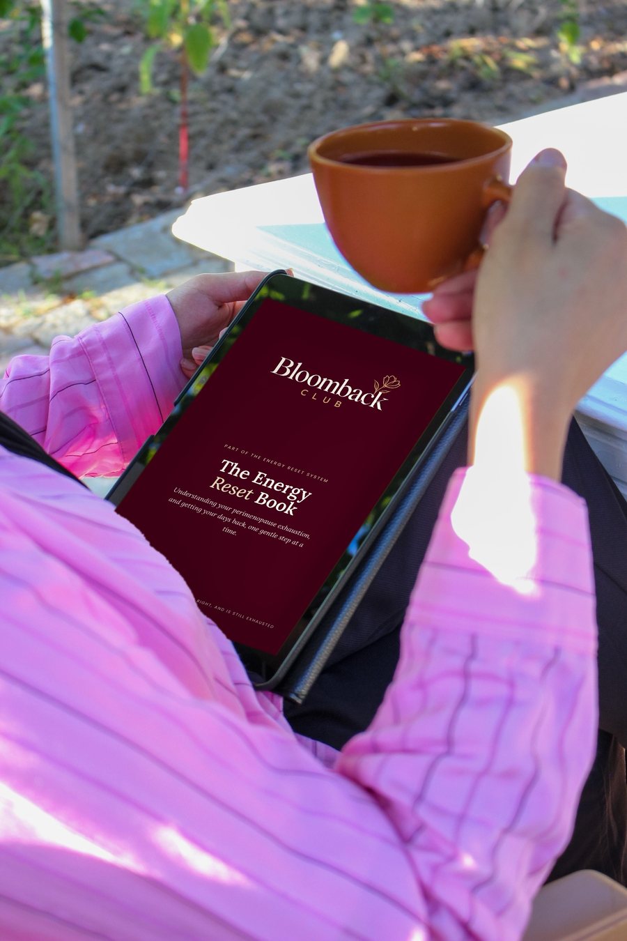 A woman with a cup of tea reading The Energy Reset Book on her tablet